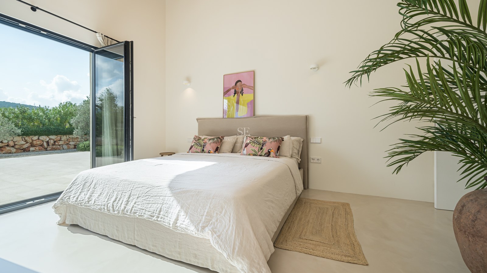 Chambre lumineuse avec baies vitrées ouvrant sur une terrasse, literie neutre et grande plante verte.