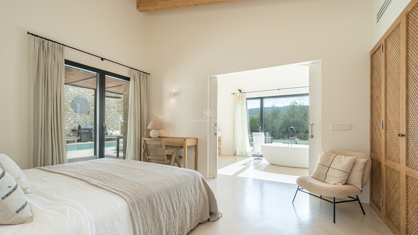 Chambre principale moderne avec poutres en bois, salle de bain attenante, baignoire îlot et accès terrasse.