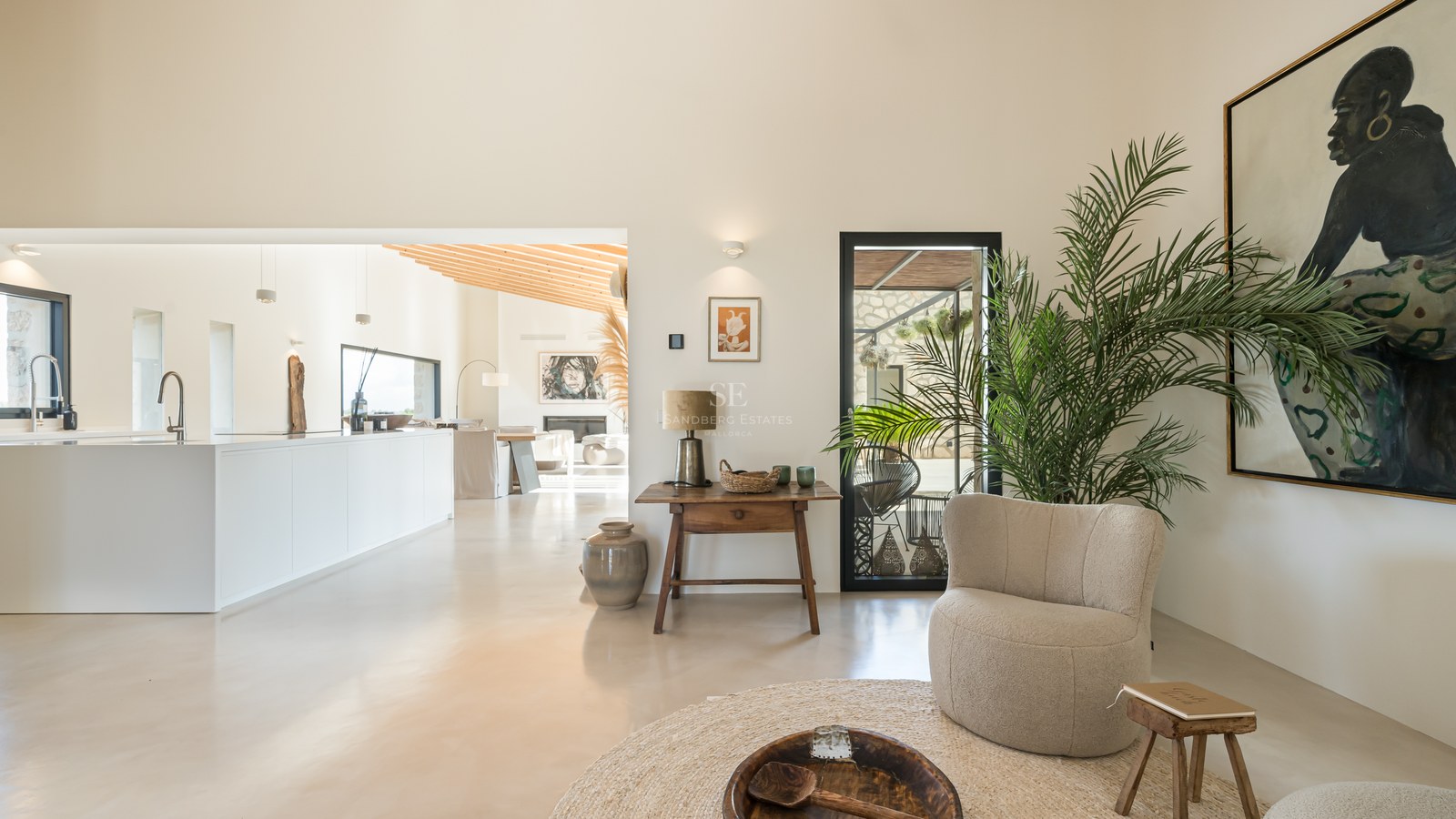 Intérieur lumineux avec sols en béton ciré, hauts plafonds, mobilier contemporain et cuisine blanche ouverte.