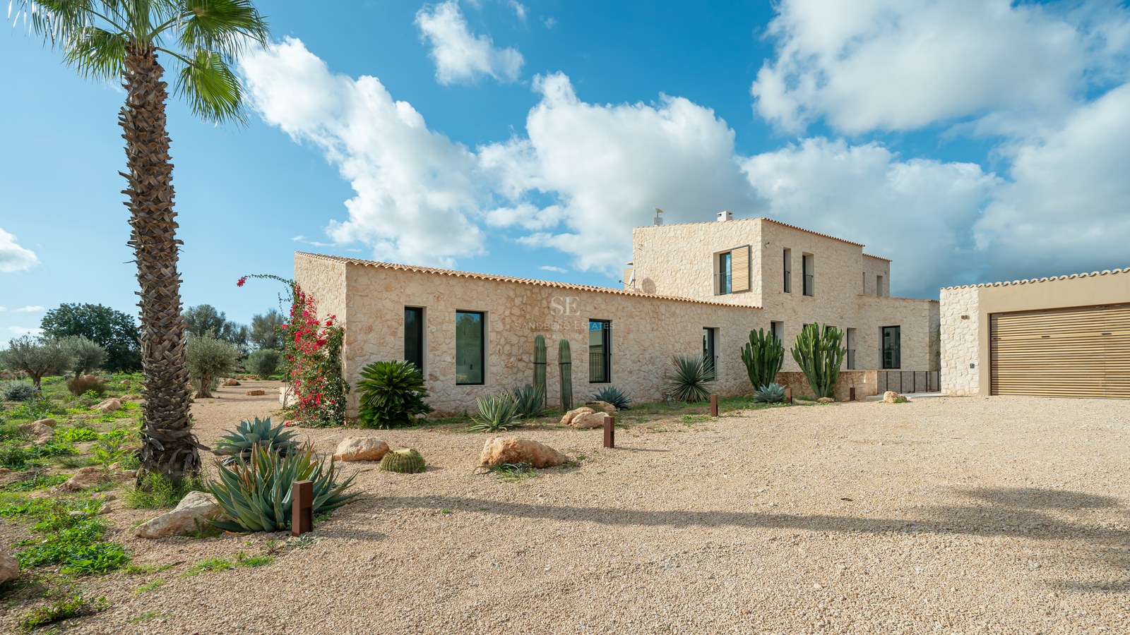 Façade en pierre naturelle d'une villa moderne avec jardin de cactus et allée en gravier sous un ciel bleu.