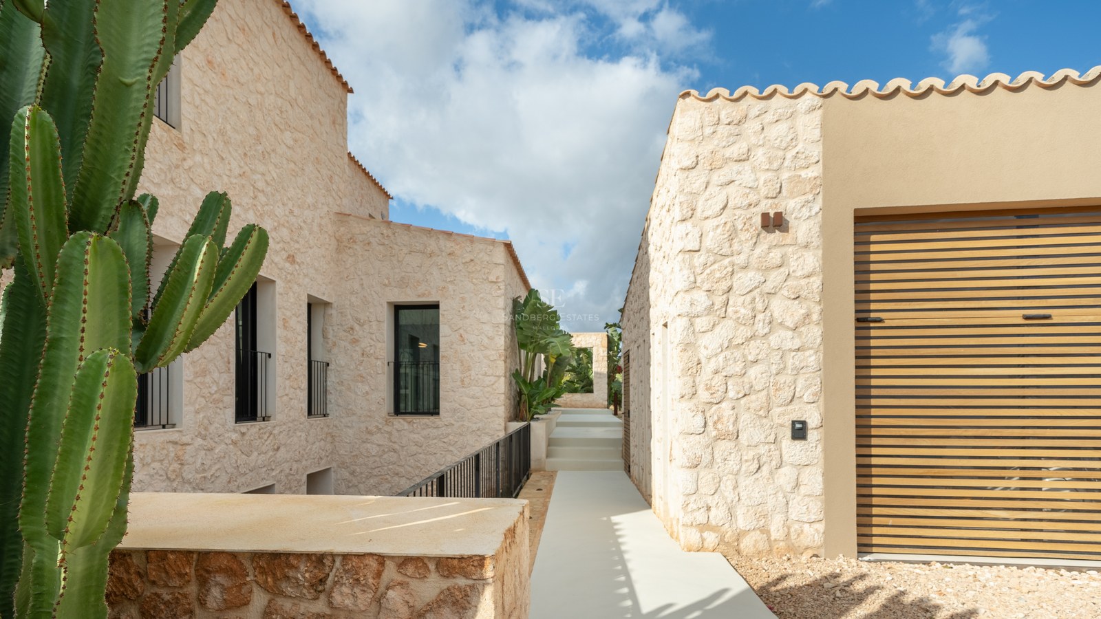 Allée minimaliste en pierre naturelle entre deux bâtiments de villas contemporaines sous un ciel bleu.
