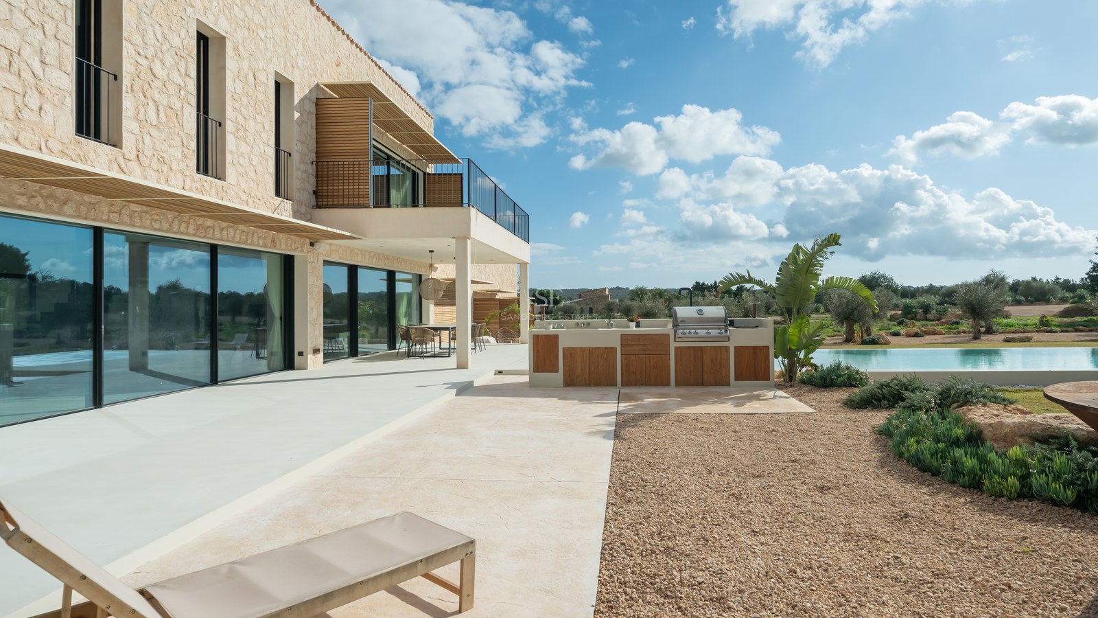 Terrasse moderne avec cuisine d'été en bois, façade en pierre naturelle et larges baies vitrées.