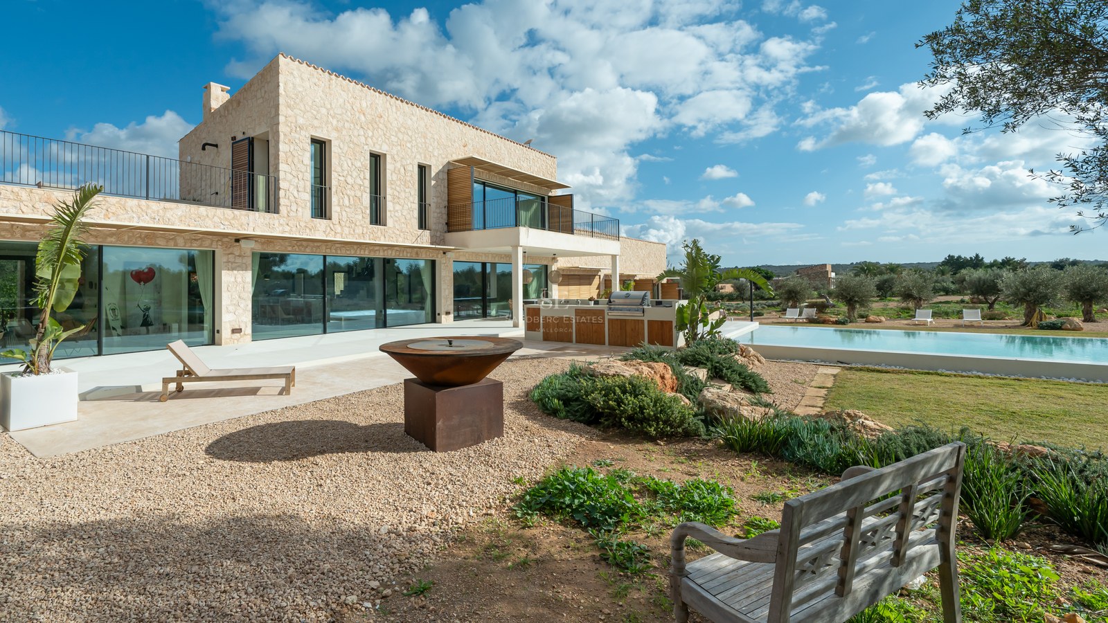 Villa moderne à deux étages avec murs en pierre naturelle, grandes baies vitrées, cuisine d'été et brasero extérieur.