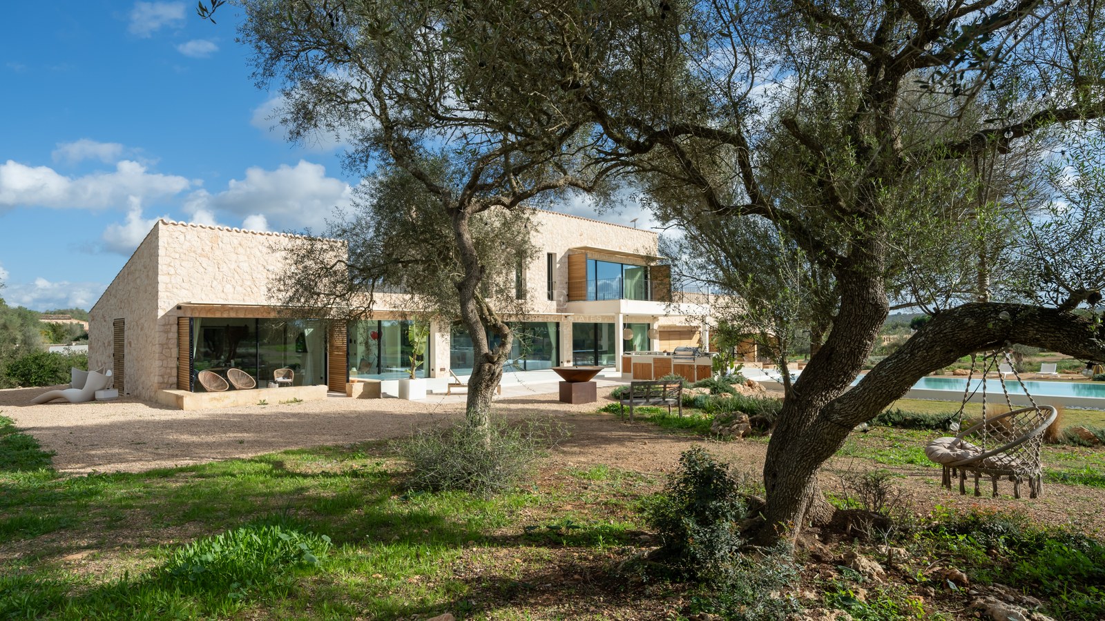 Villa contemporaine de deux étages avec de grandes baies vitrées vue à travers des oliviers centenaires.