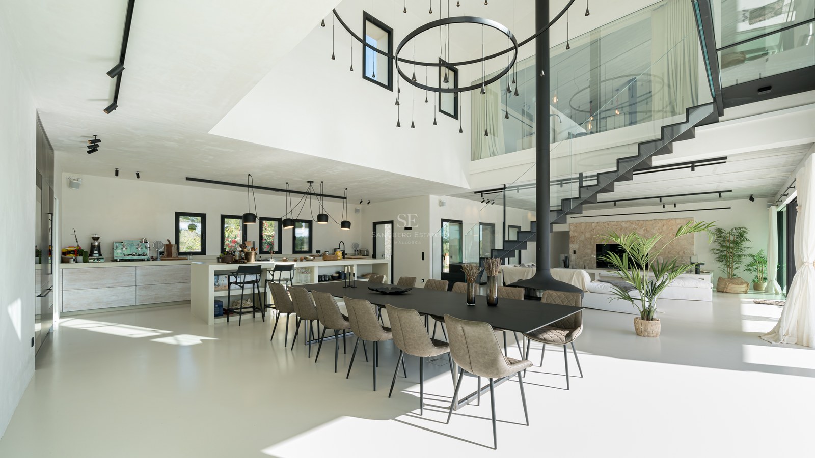 Salle à manger moderne avec grande table noire, cheminée suspendue et mezzanine vitrée sous plafond haut.