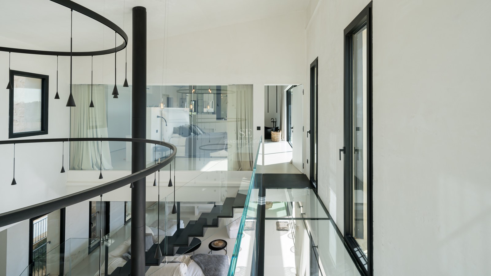 Couloir intérieur moderne avec passerelle en verre, escalier noir et grandes fenêtres dans une villa contemporaine.
