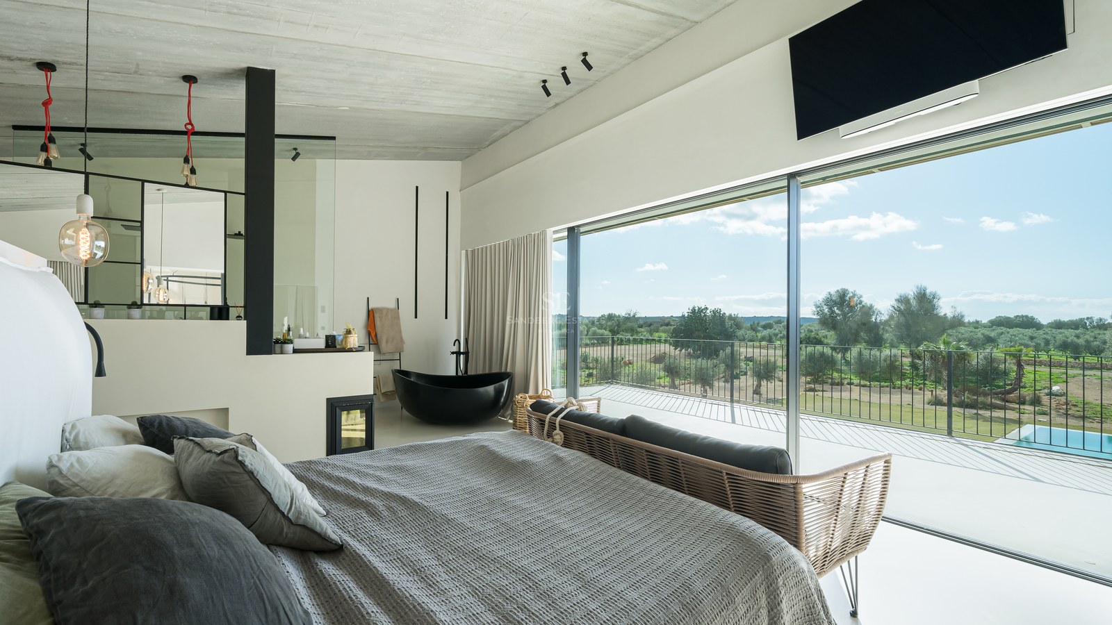 Chambre de maître moderne avec baignoire noire, cheminée et baies vitrées donnant sur la campagne.