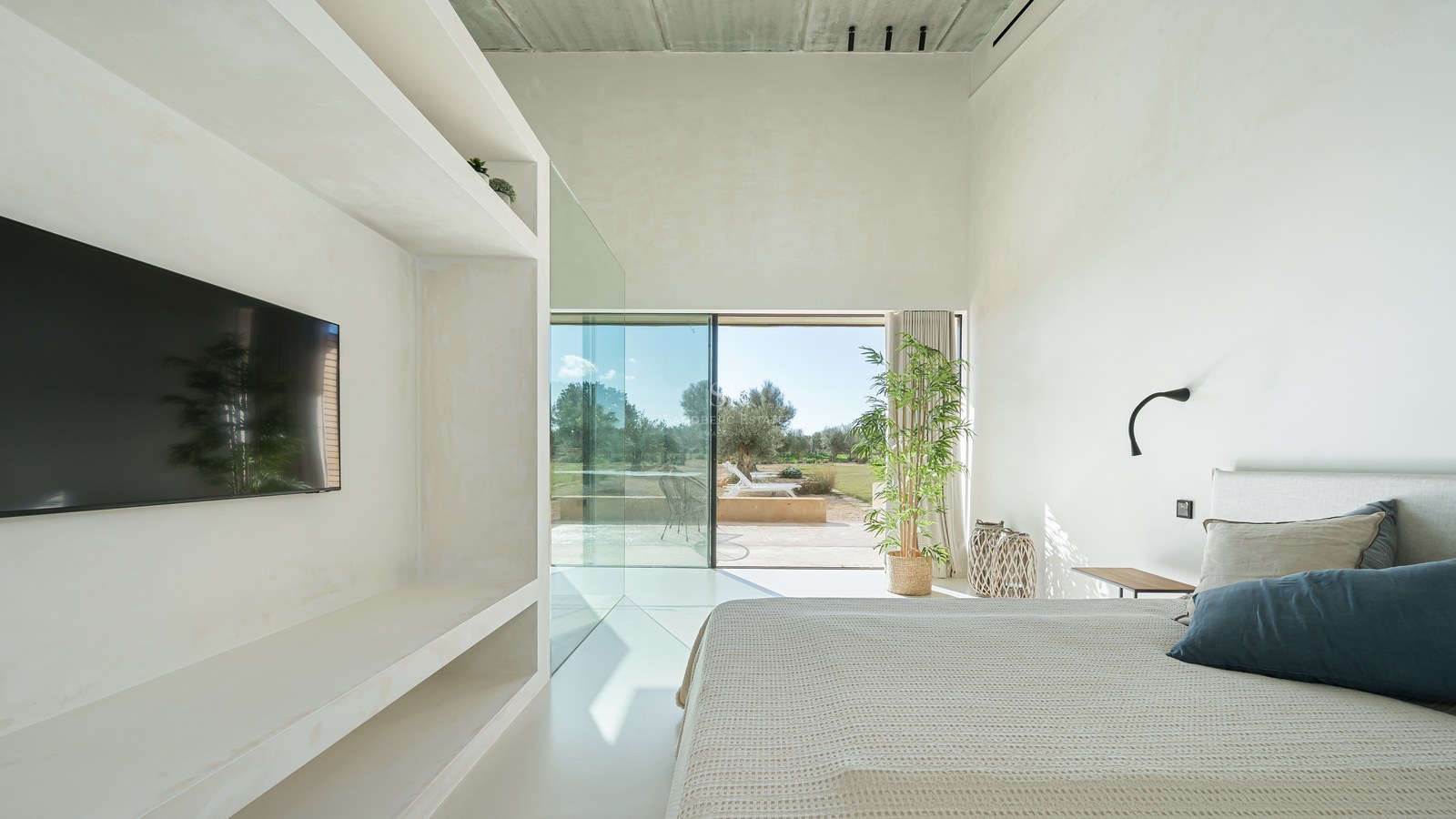 Chambre blanche minimaliste avec de grandes baies vitrées ouvrant sur une terrasse ensoleillée et un jardin.