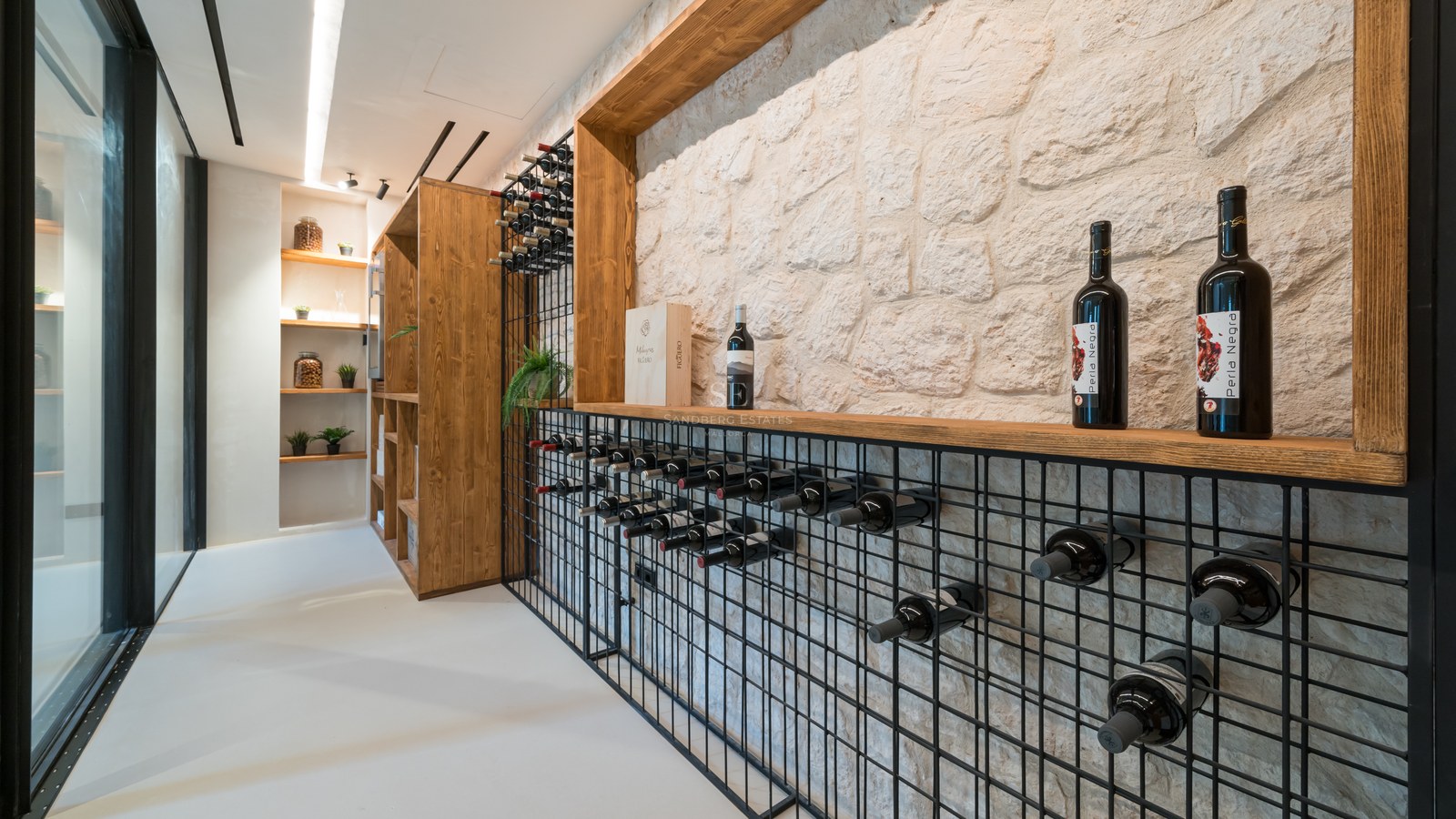 Cave à vin moderne avec mur en pierre blanche, casiers en métal noir et finitions en bois clair.