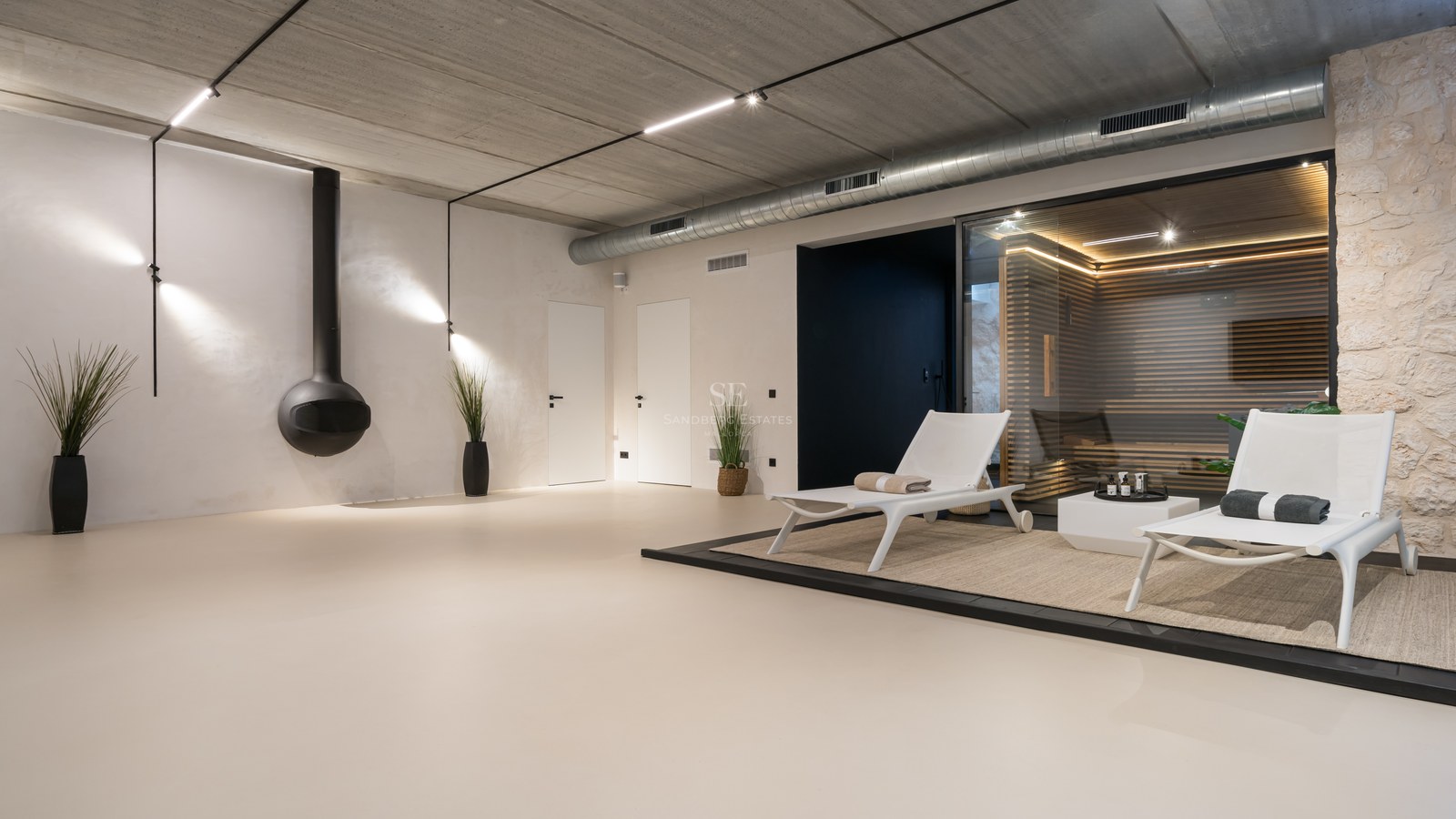 Spa intérieur minimaliste avec sauna en bois et verre, chaise longue blanche et finitions industrielles.