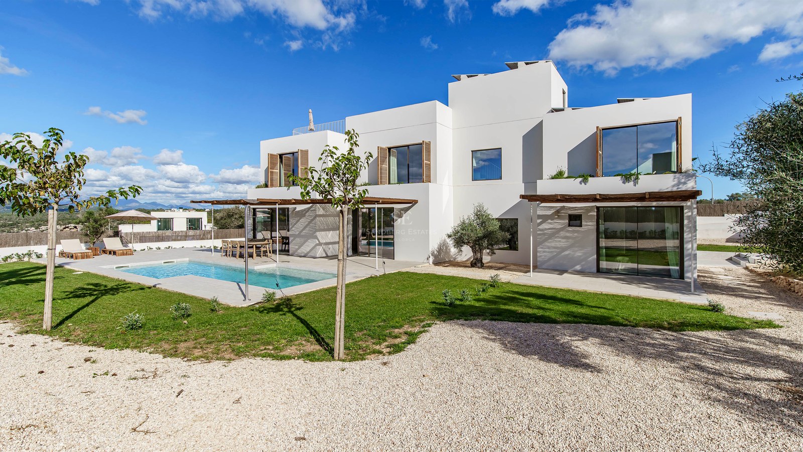 Modern vit villa med rektangulär pool, träluckor och anlagd trädgård under en klarblå himmel.