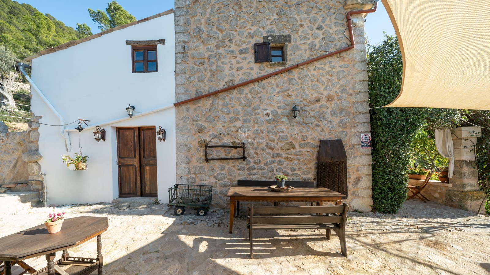 Mur en pierre authentique, porte en bois, volets et table à manger extérieure sur une terrasse ensoleillée.