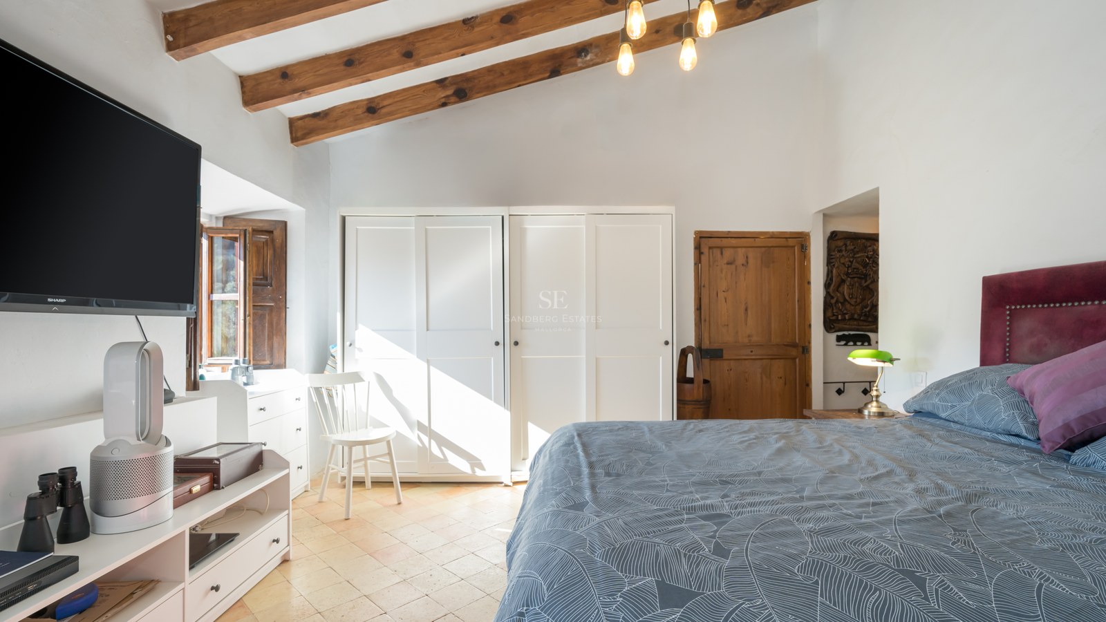 Chambre lumineuse avec poutres de plafond en bois, armoires encastrées blanches et parquet clair.