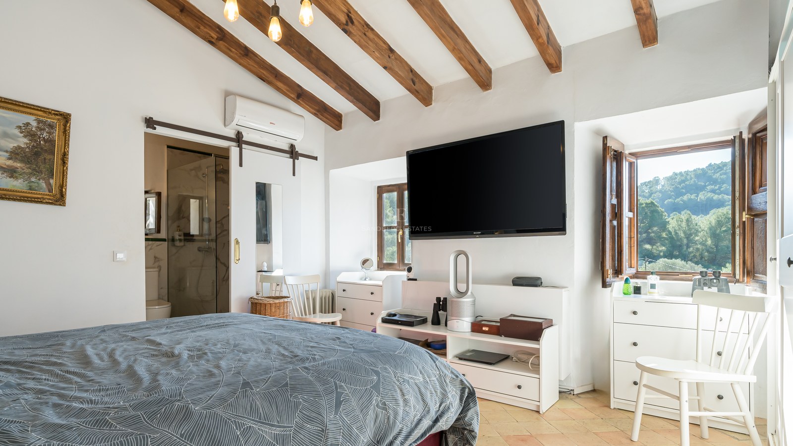 Chambre disposant de poutres en bois au plafond, d'un téléviseur mural et d'une porte coulissante blanche.