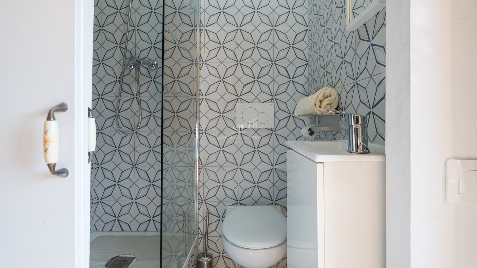 Salle de bains contemporaine avec carreaux géométriques bleus et blancs, paroi de douche en verre et vasque blanche.