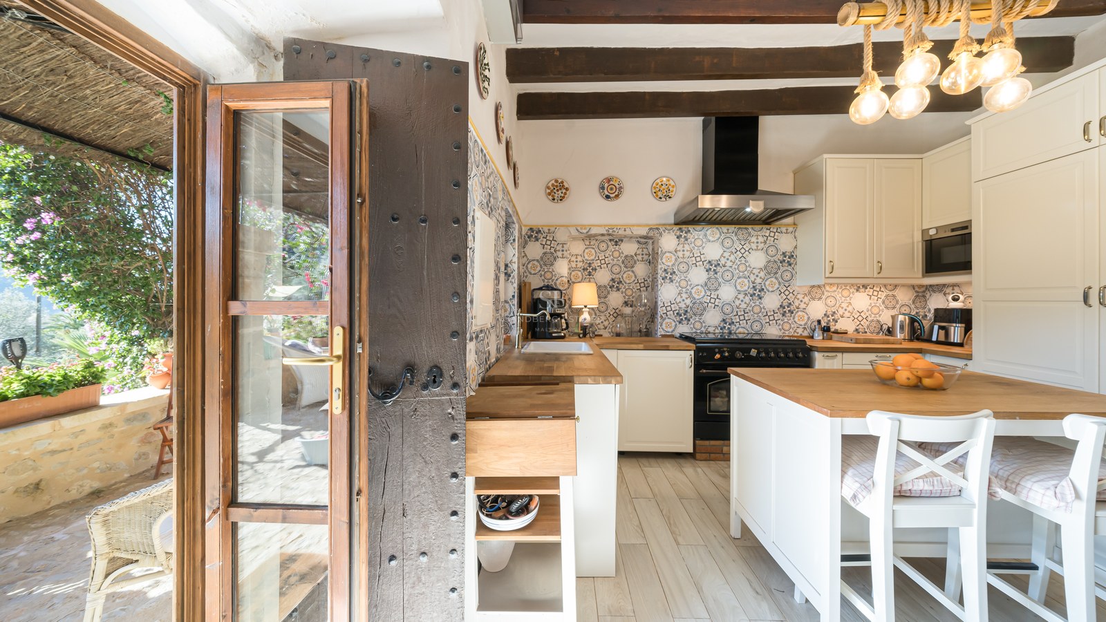 Cuisine rustique avec crédence en carreaux de ciment, poutres en bois sombre et porte traditionnelle cloutée.