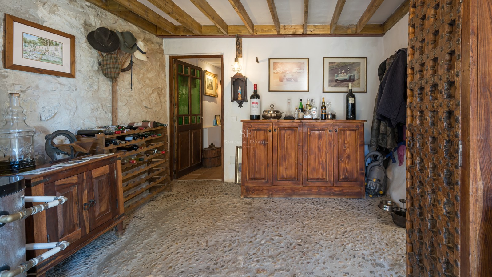 Intérieur d'une cave à vin rustique avec poutres apparentes, murs en pierre et buffet en bois massif.