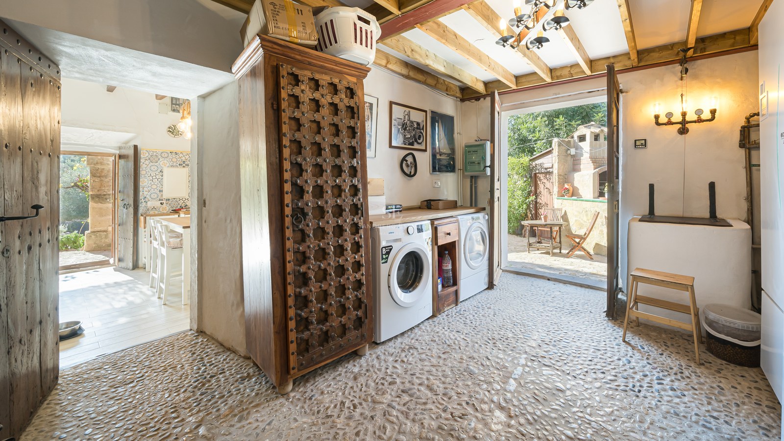 Espace buanderie avec sol en galets, armoire en bois sculpté et accès direct vers l'extérieur.