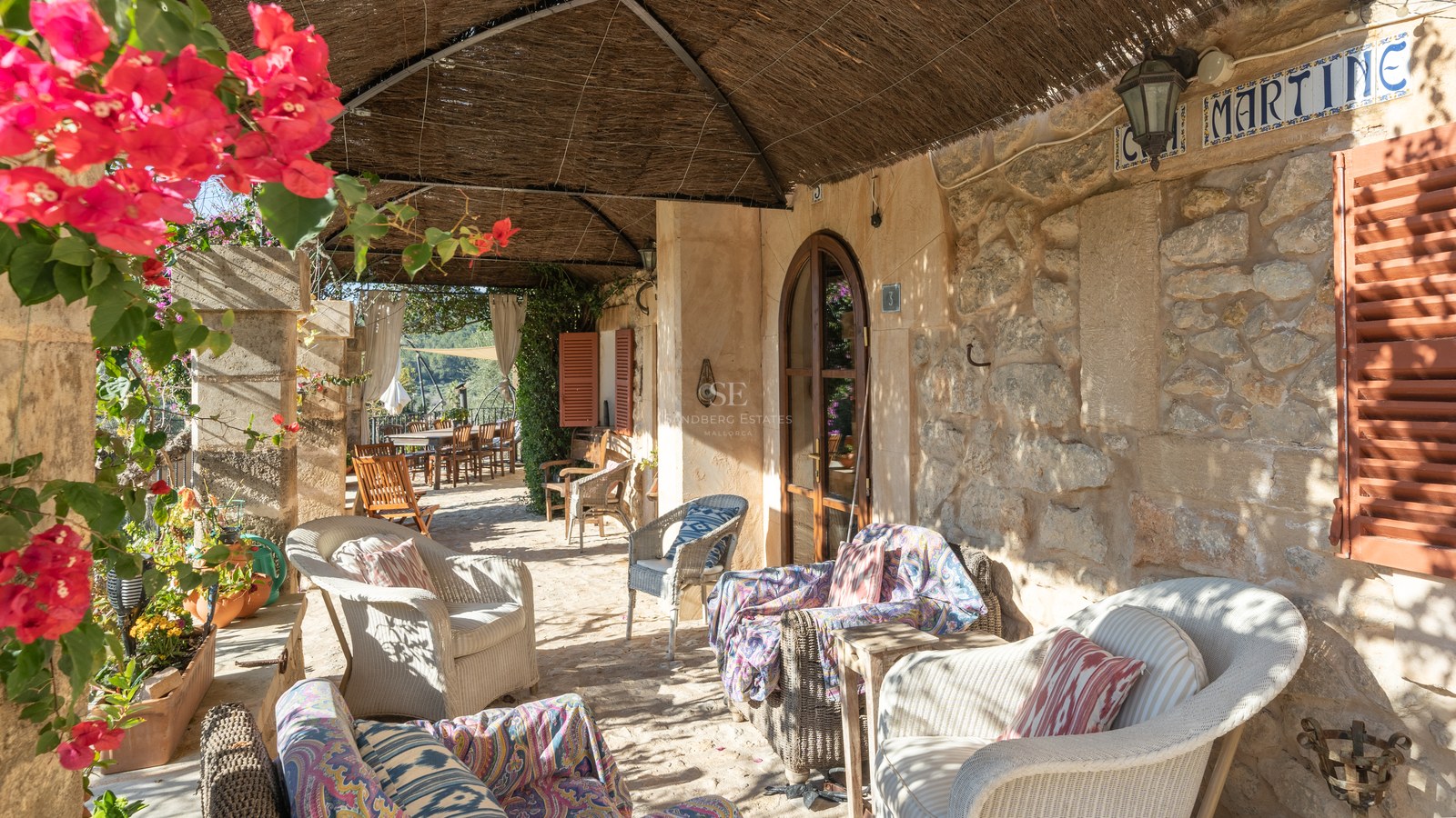 Une terrasse couverte avec des murs en pierre, des fauteuils en osier et un toit traditionnel en canisse.