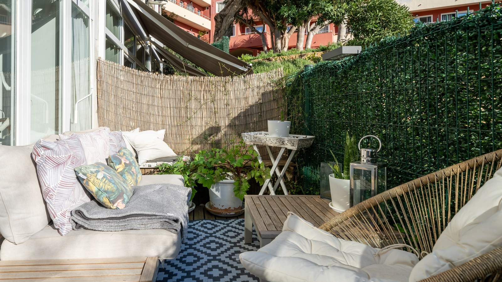 Sunny terrace featuring comfortable sofas, a geometric rug, and bamboo privacy screening in a coastal setting.