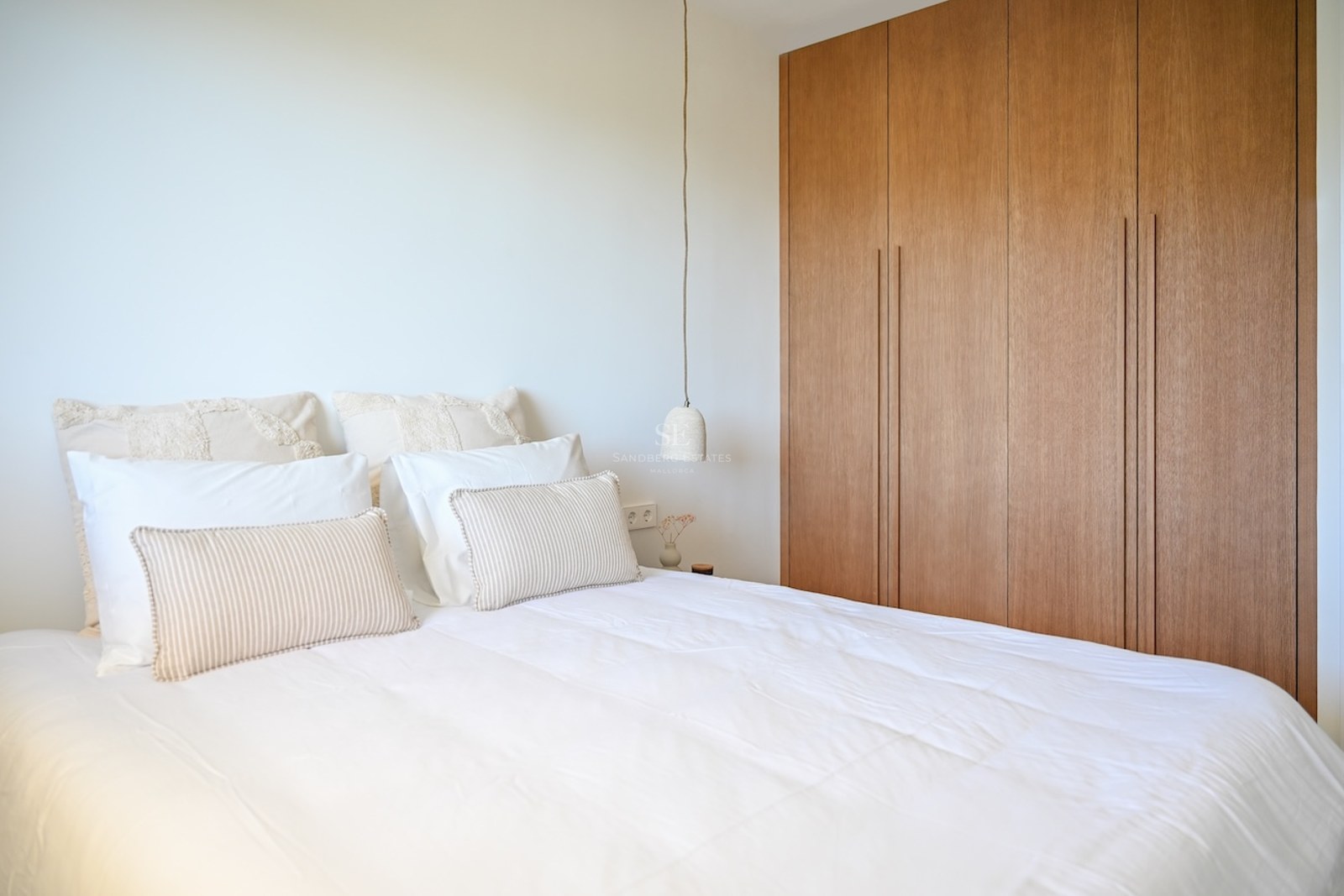 Dormitorio luminoso con cama blanca, cojines a rayas y grandes armarios empotrados de madera de suelo a techo.