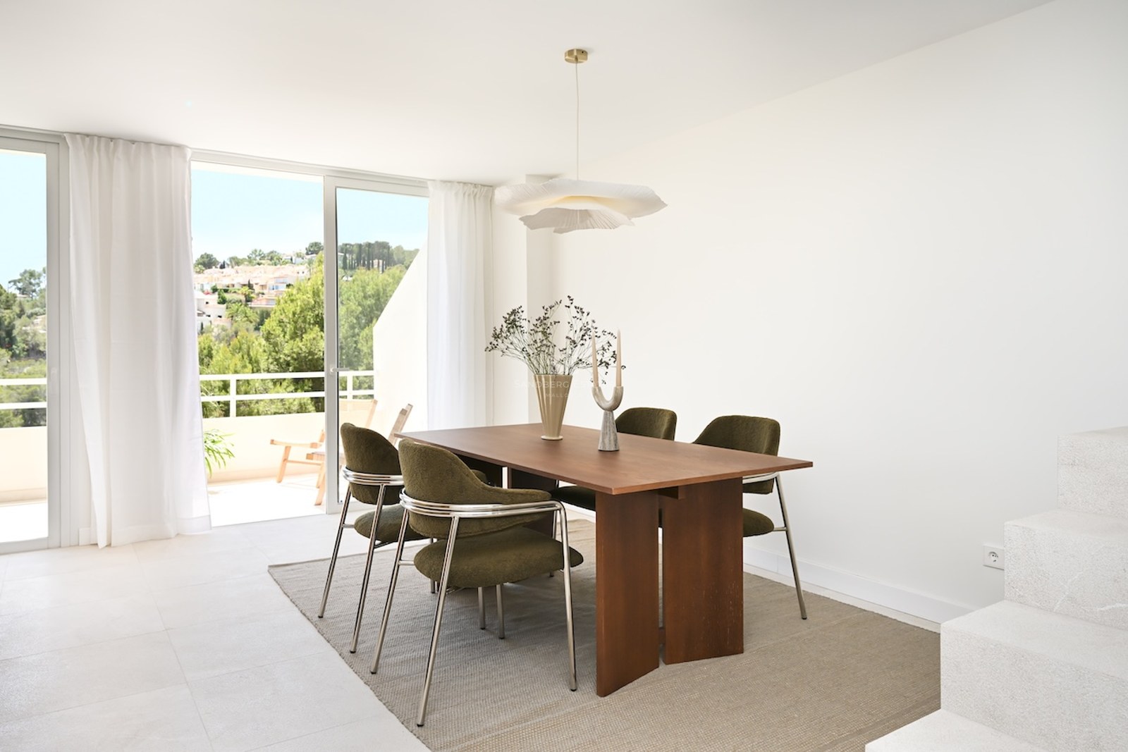 Comedor moderno con mesa de madera, sillas verde oliva y grandes ventanales con acceso a una terraza soleada.
