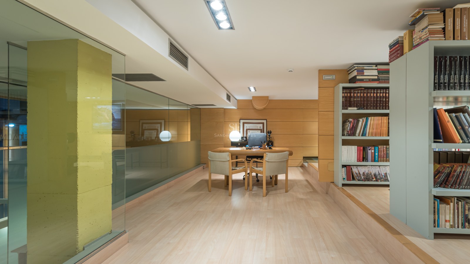 Modern home office featuring wood-paneled walls, a minimalist desk with two chairs, and floor-to-ceiling glass partitions.