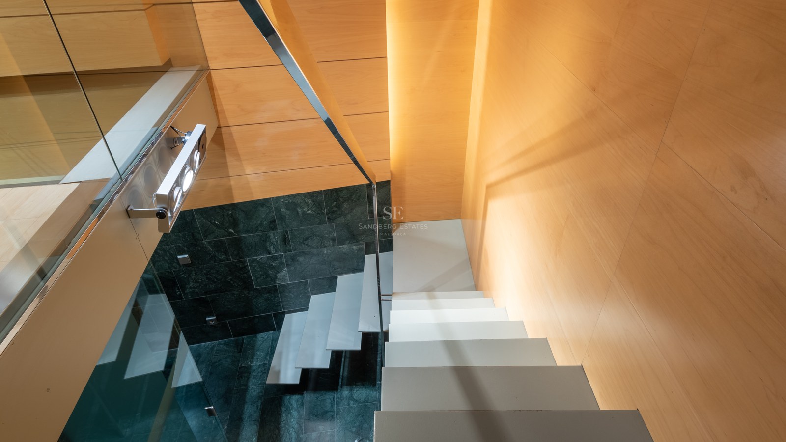 High-angle view of a modern staircase featuring white floating steps, dark green marble walls, and warm wood paneling.