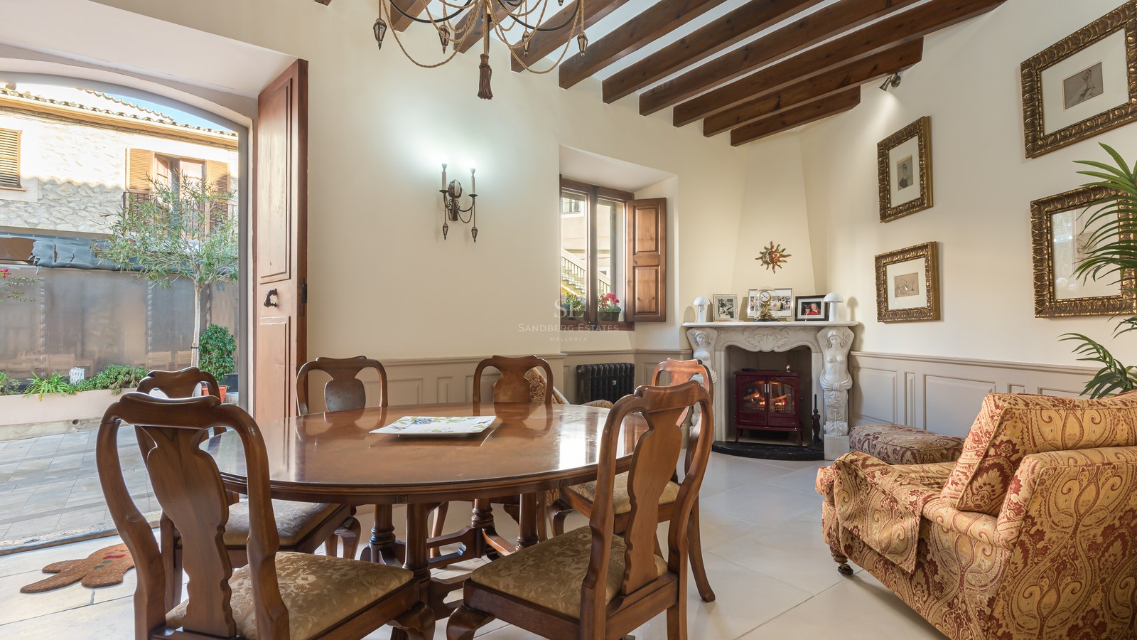 Salle à manger élégante avec table en bois, poutres apparentes et cheminée ornée menant à un patio.