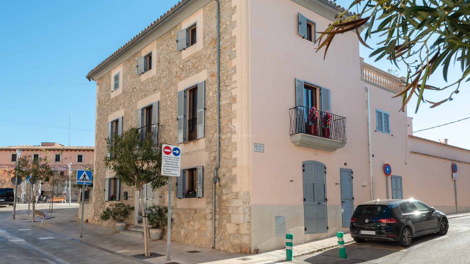 Bâtiment d'angle de trois étages avec façade en pierre naturelle, volets majorquins gris et balcons en fer forgé.