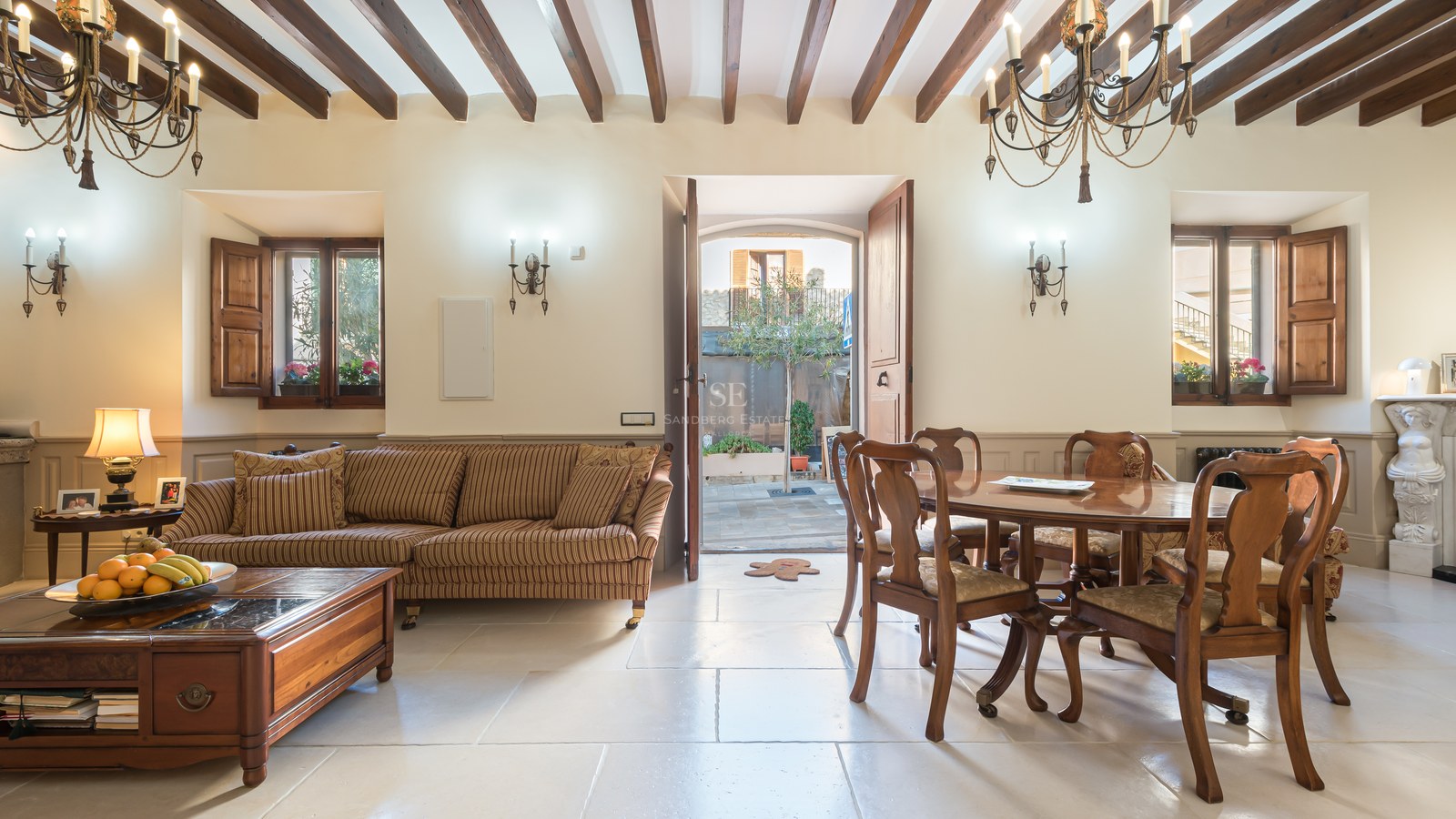 Intérieur rustique avec un canapé à rayures, une table à manger en bois, des sols en pierre et des poutres apparentes.