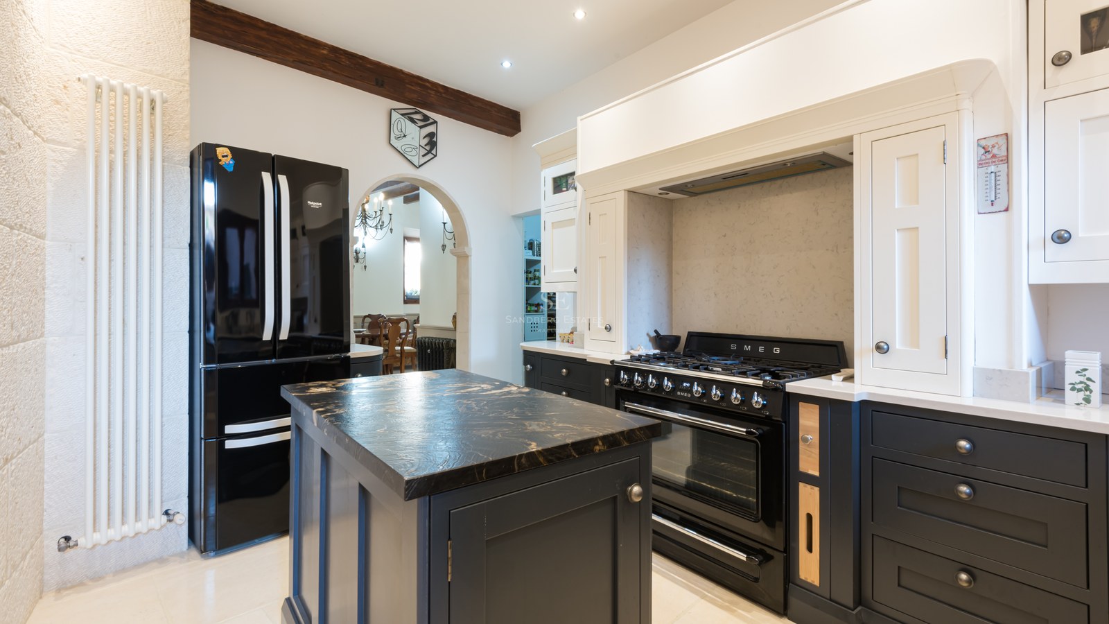 Cuisine moderne rustique avec four SMEG noir, îlot en marbre, poutres en bois et murs en pierre naturelle.