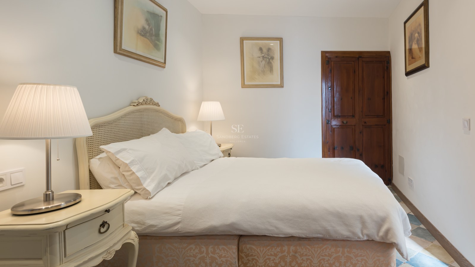 Chambre chaleureuse avec lit blanc, tête de lit en canne, lampes de chevet et porte en bois sombre.