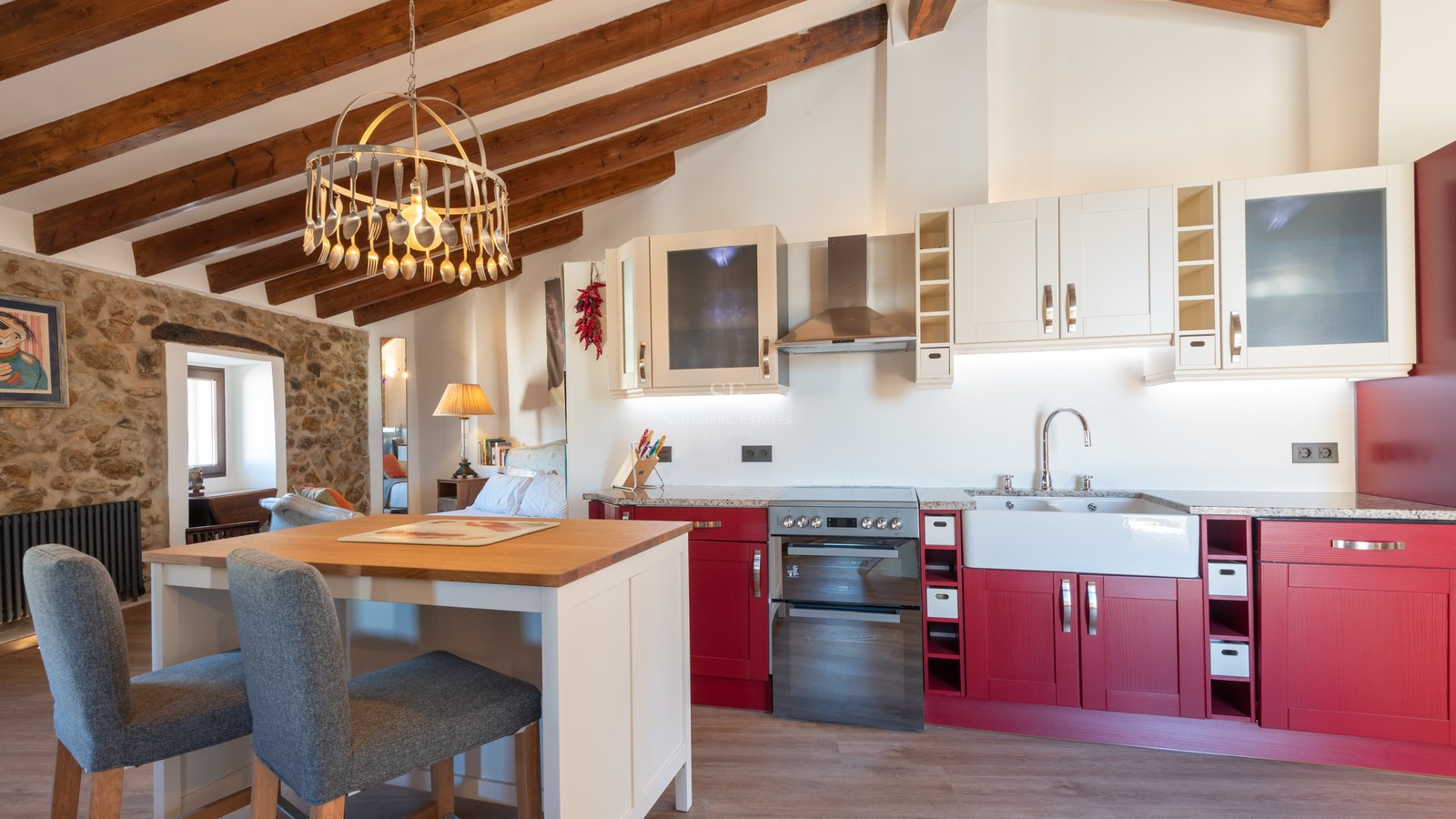Cuisine avec placards rouges, poutres en bois apparentes et mur en pierre naturelle avec îlot central.