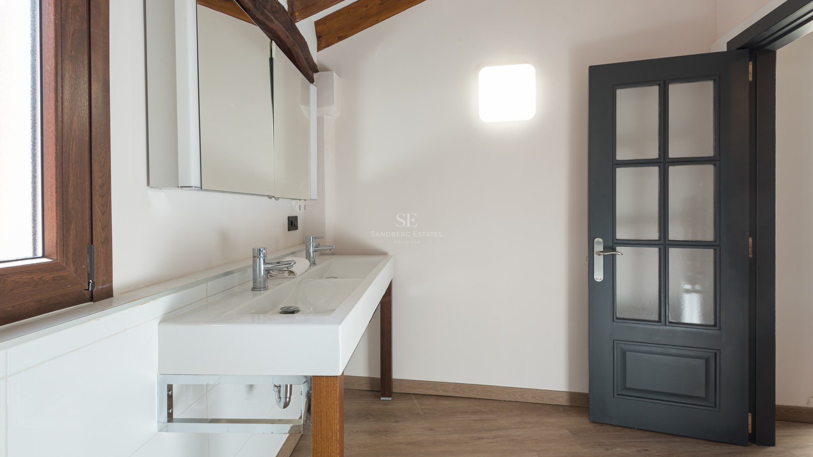 Salle de bain avec double lavabo blanc, poutres apparentes, porte gris foncé et armoire de toilette miroir.