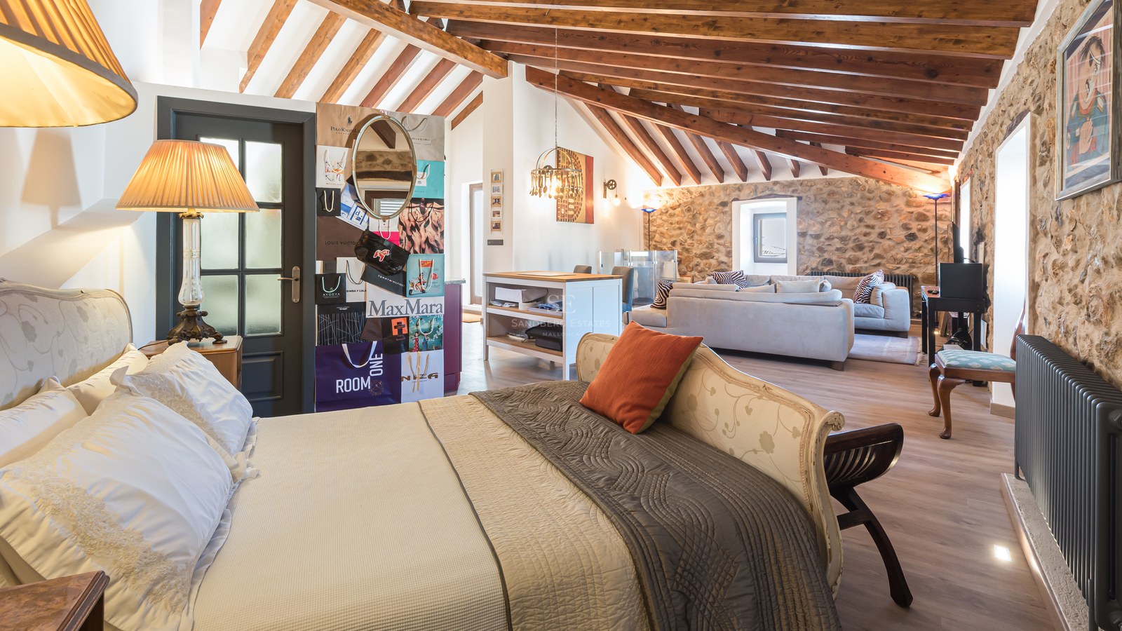 Chambre de luxe avec poutres en bois apparentes, murs en pierre naturelle et coin salon intégré.