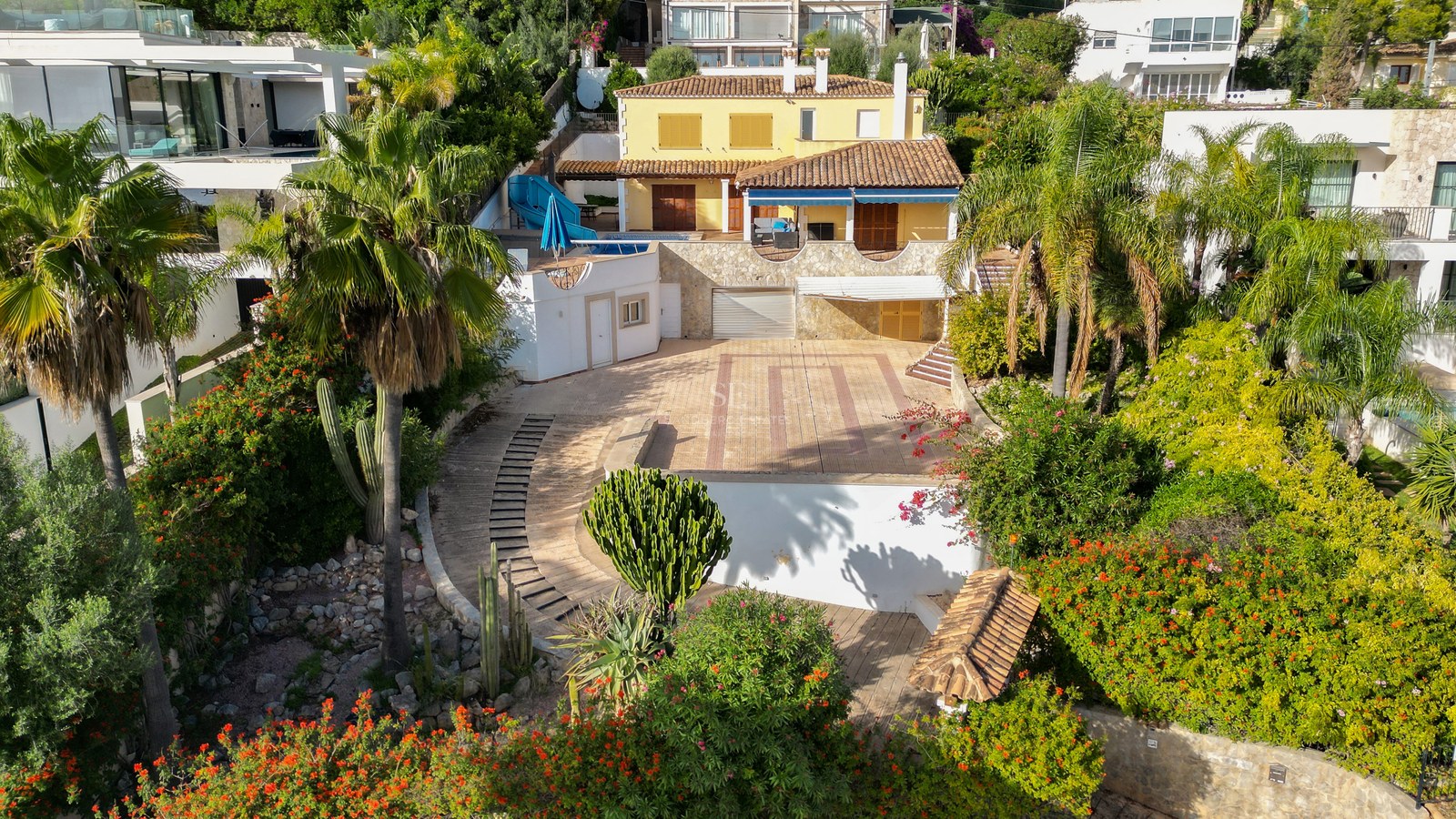 Luftaufnahme einer gelben mediterranen Villa mit Pool, Terrakottadach und üppiger tropischer Bepflanzung.