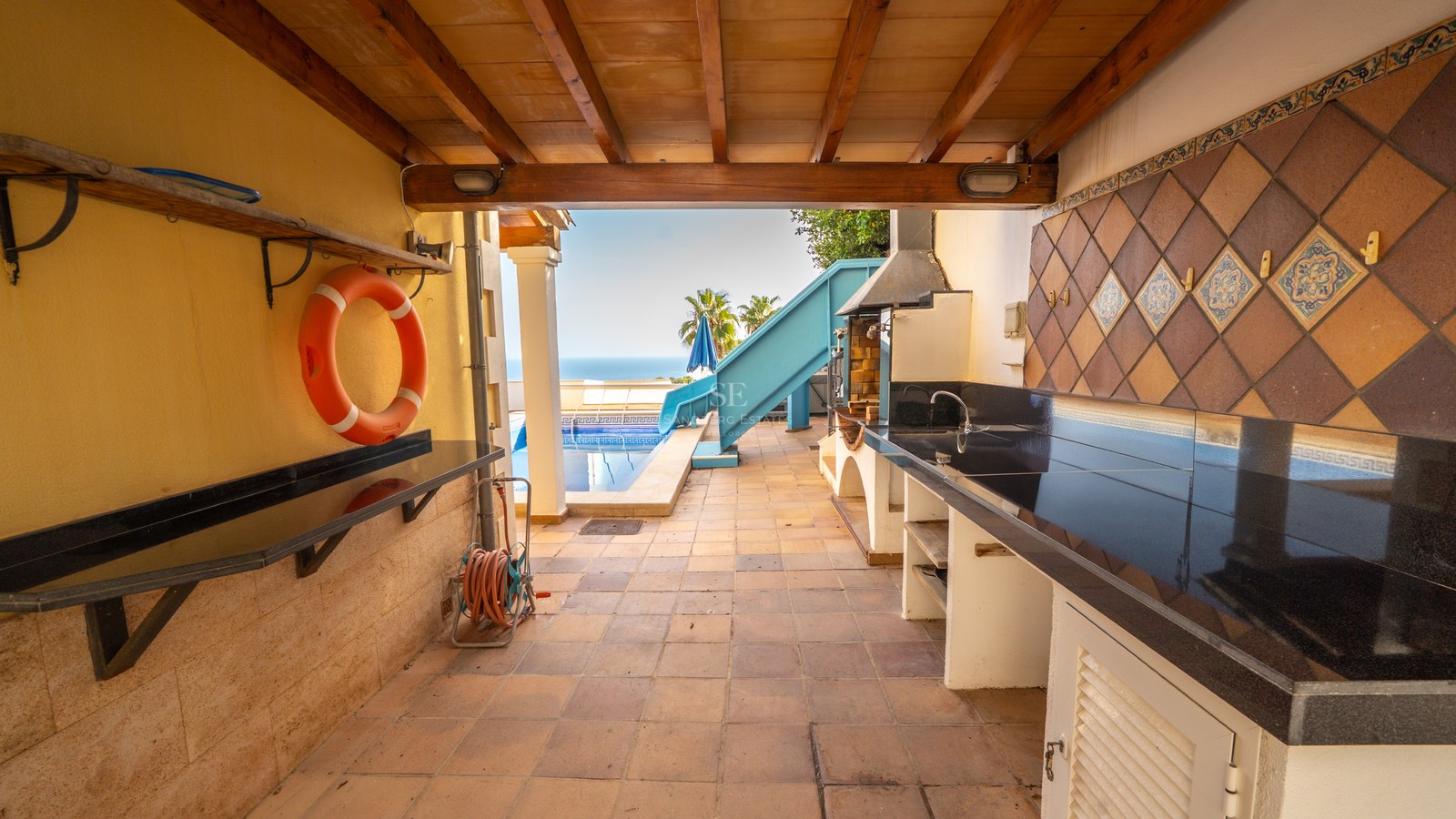 Außenküche auf einer überdachten Terrasse mit Grill, schwarzen Arbeitsplatten und Blick auf den Pool und das Meer.