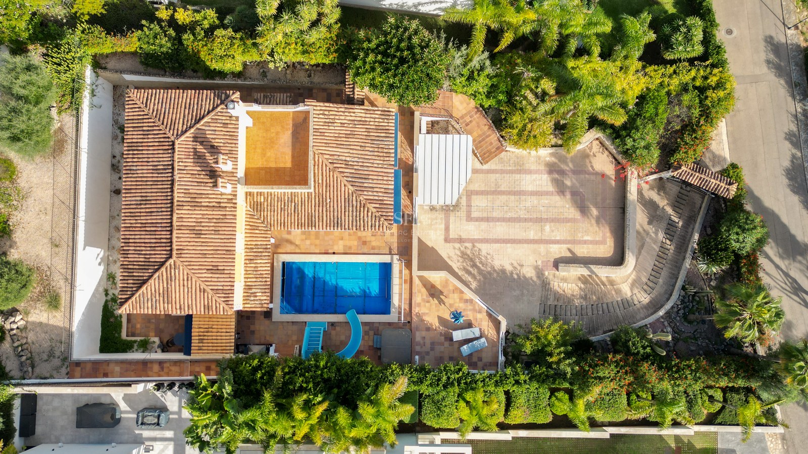 Vogelperspektive einer Villa mit Terrakottadach, blauem Pool mit Rutsche und üppigen grünen Gärten.