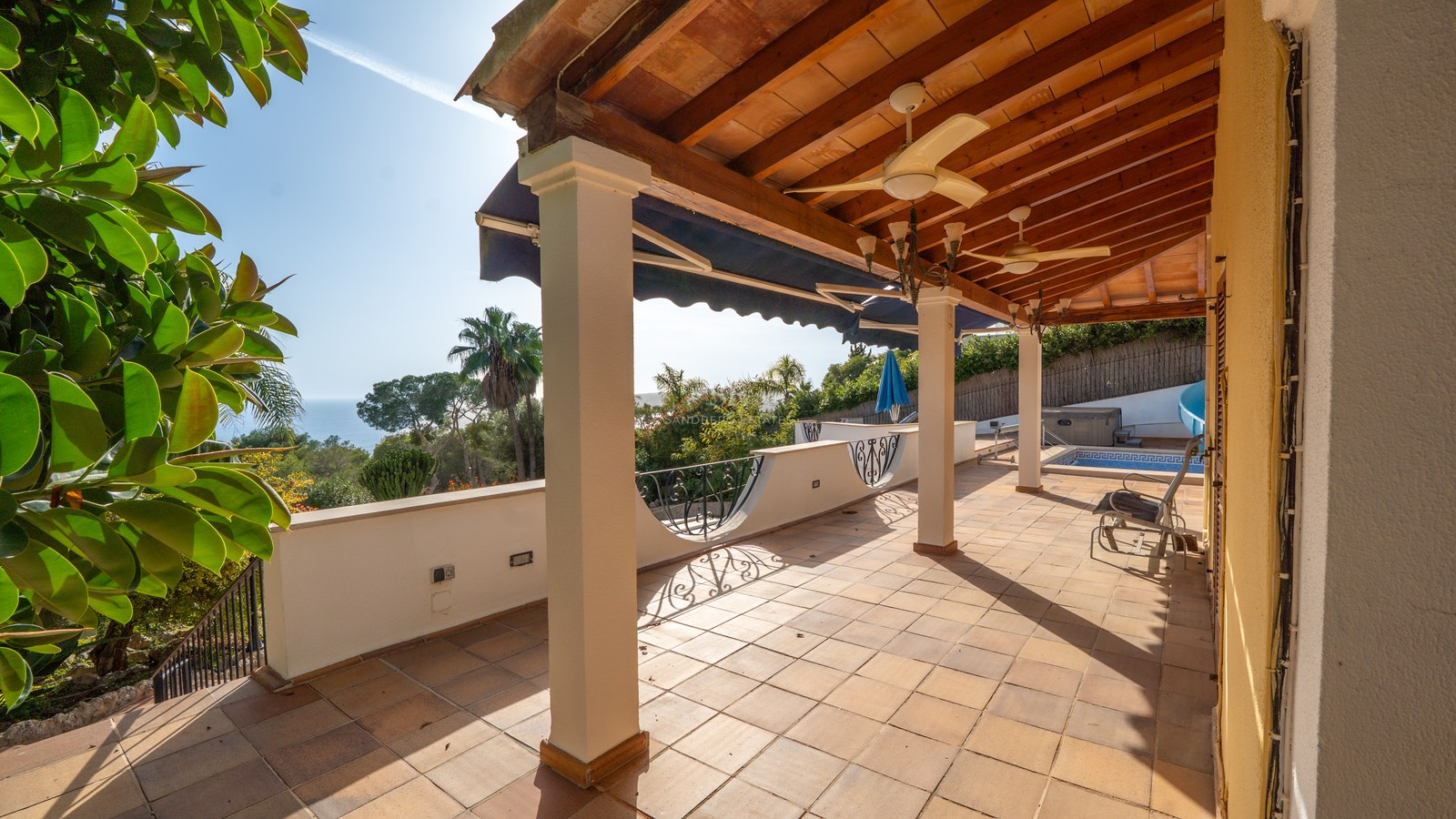 Große überdachte Terrasse mit weißen Säulen, Terrakottaboden und Panoramablick auf das Meer.
