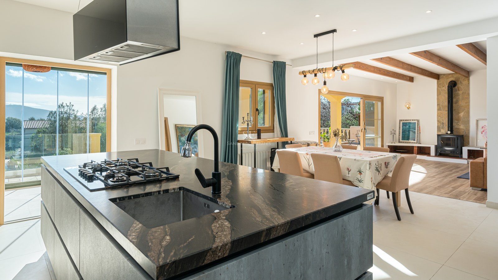 Isla de cocina moderna con encimera de piedra oscura que da a un comedor y sala de estar con chimenea.