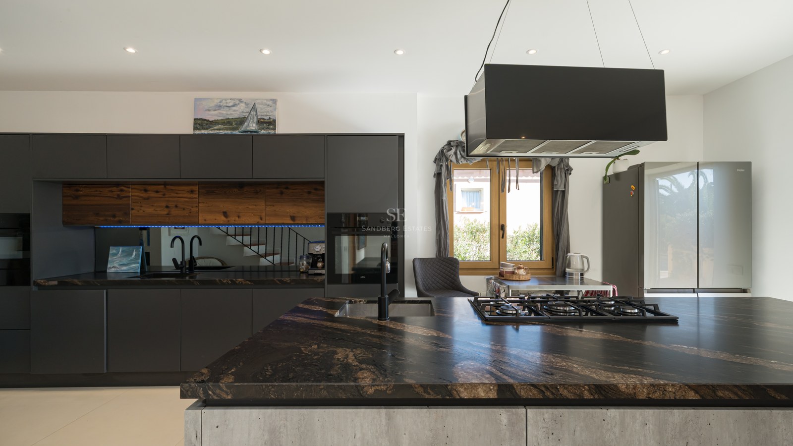 Cocina moderna con isla de mármol oscuro, armarios negros mate y detalles en madera.