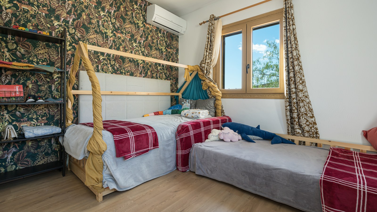 Dormitorio infantil con cama de madera en forma de casita, papel de jungla y luz natural.