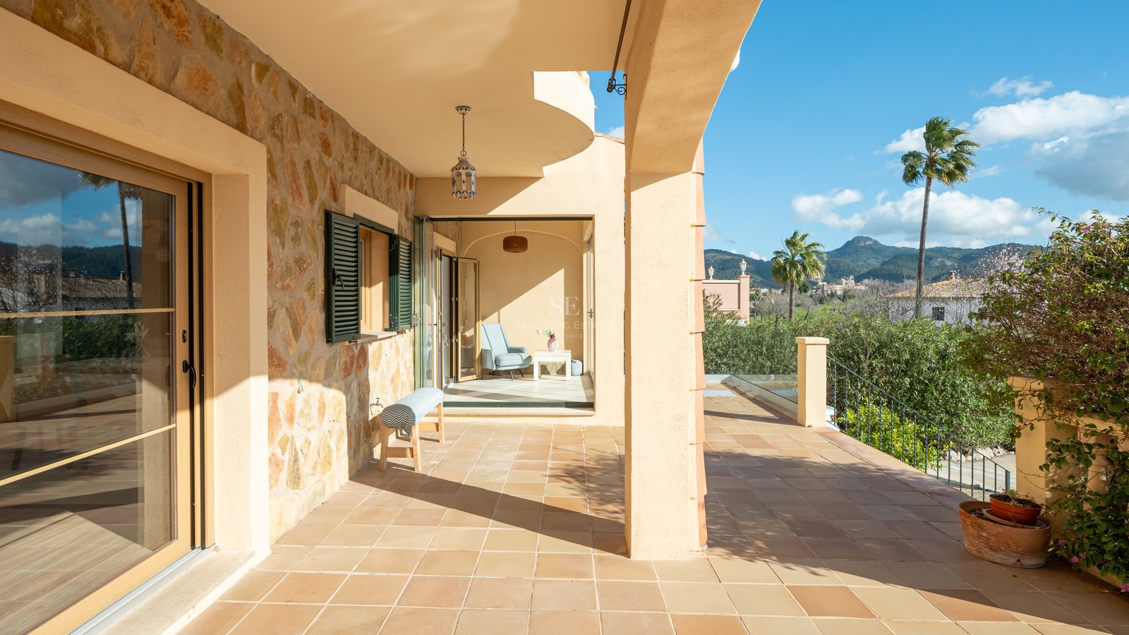 Terraza cubierta con suelos de terracota y pared de piedra natural con vistas a colinas verdes y montañas.