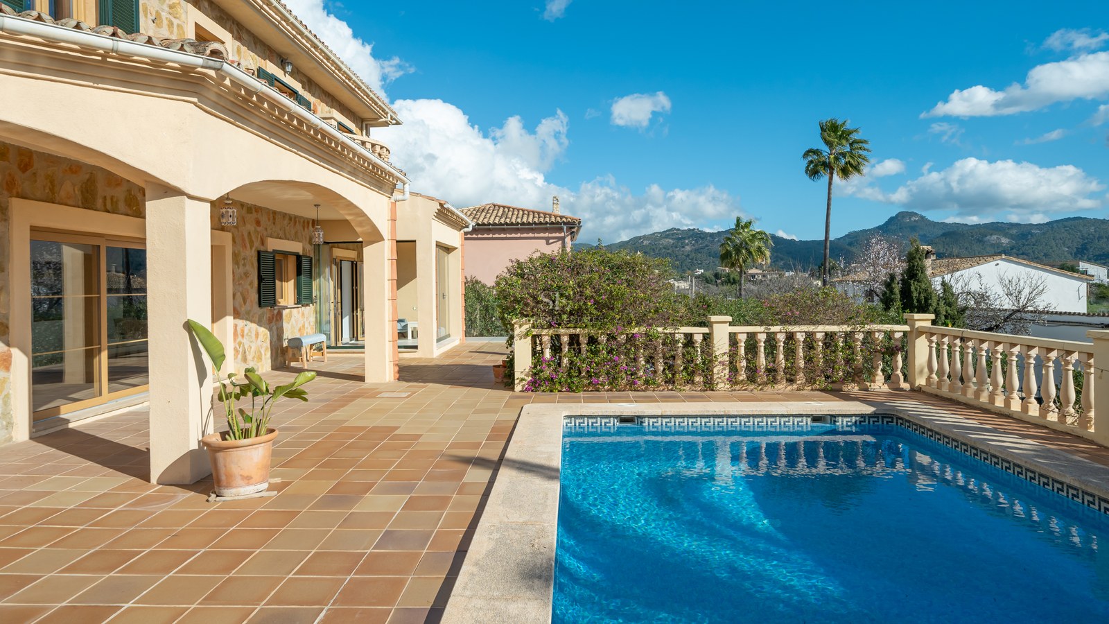 Terraza de villa de lujo con piscina de azulejos azules, suelo de terracota y vistas a las montañas.