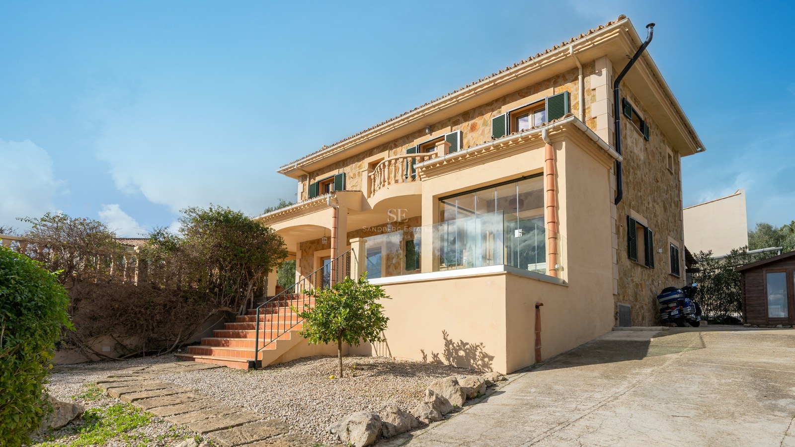 Villa mediterránea de dos plantas con muros de piedra natural, tejado de terracota y terraza acristalada.