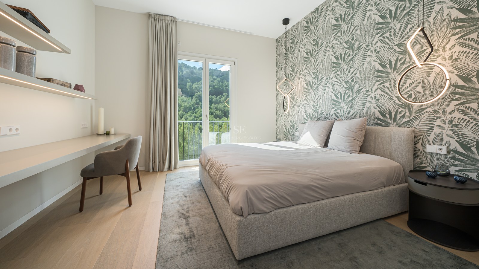 Dormitorio contemporáneo con papel pintado botánico, cama tapizada, escritorio integrado y balcón con vistas a colinas.