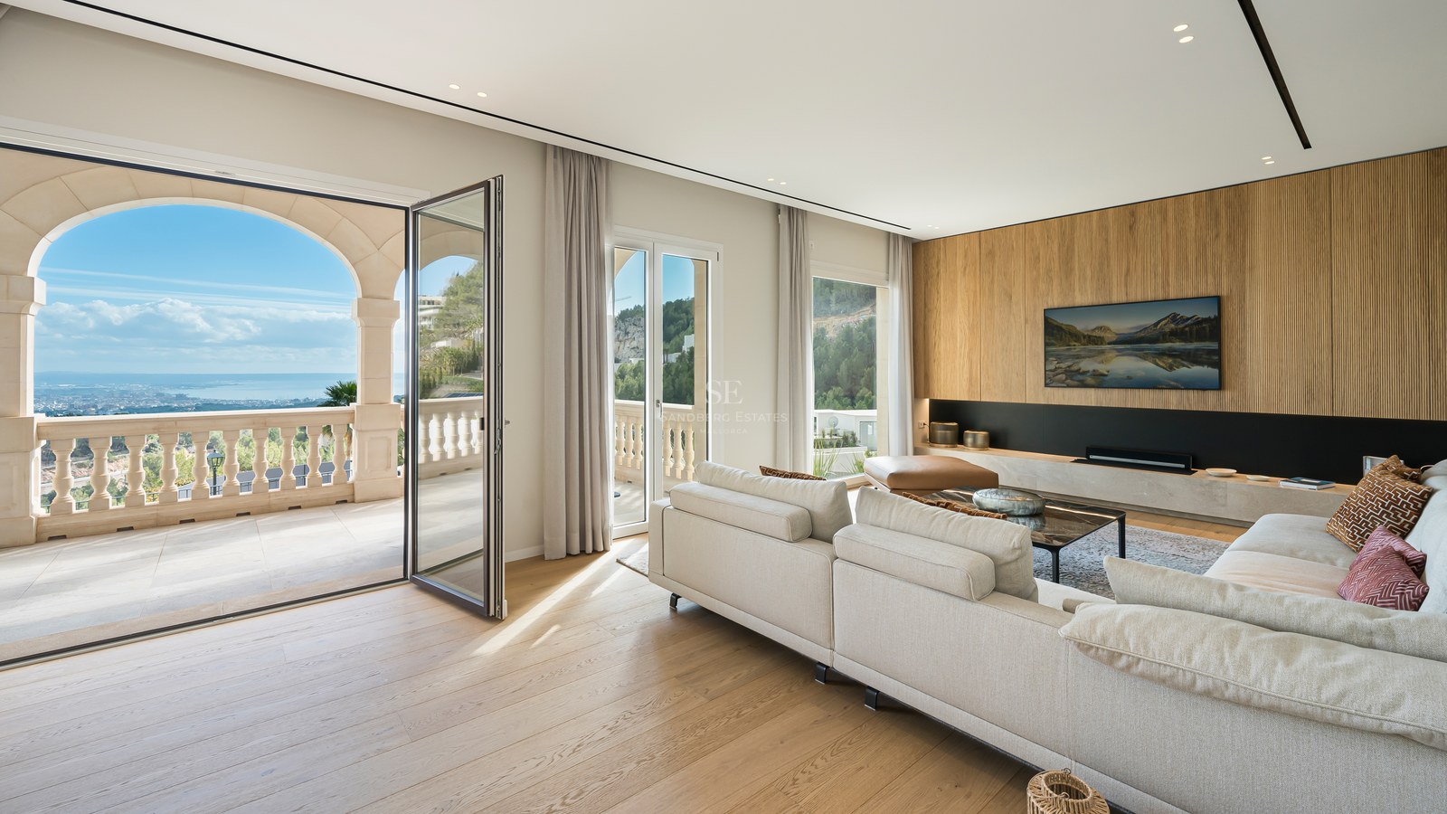 Salón espacioso con suelos de roble, sofá crema y grandes puertas de cristal que dan a una terraza con vistas al mar.
