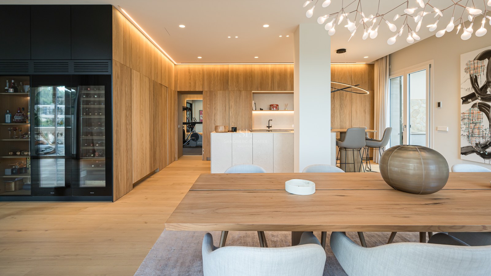 Comedor moderno con mesa de roble, vinoteca de lujo e iluminación LED integrada en una vivienda de concepto abierto.