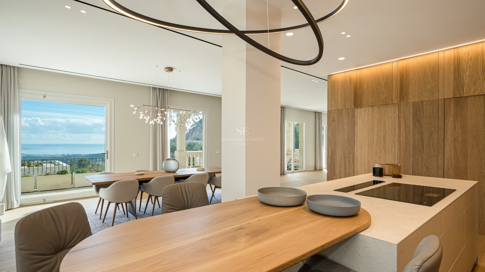Isla de cocina moderna con encimera de piedra y barra de roble con vistas al comedor y al mar Mediterráneo.